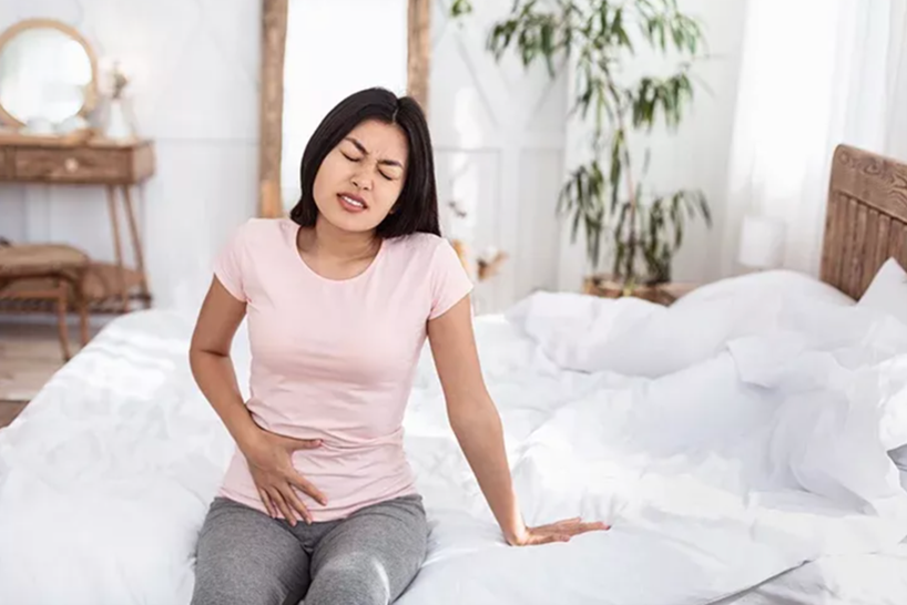 woman sitting on bed with hand on stomach with painful face