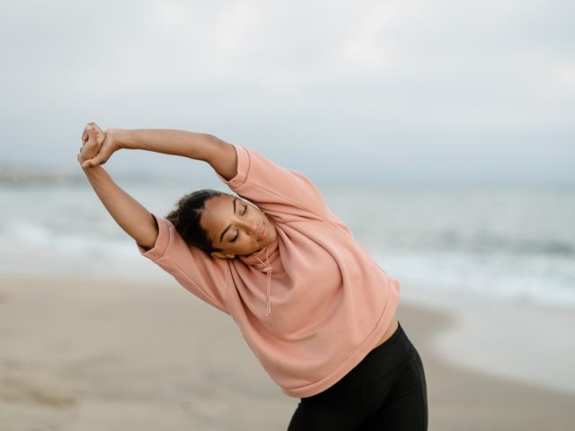Lady stretching with arms overhead on a beach