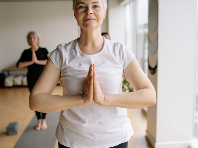 Lady with hands in prayer position doing tai chi. In exercise room, mats on ground.