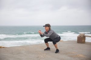 Lady squatting exercise standing on concrete looking over the ocean and beach