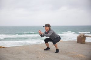Lady in active wear at beach doing squats with hat on.