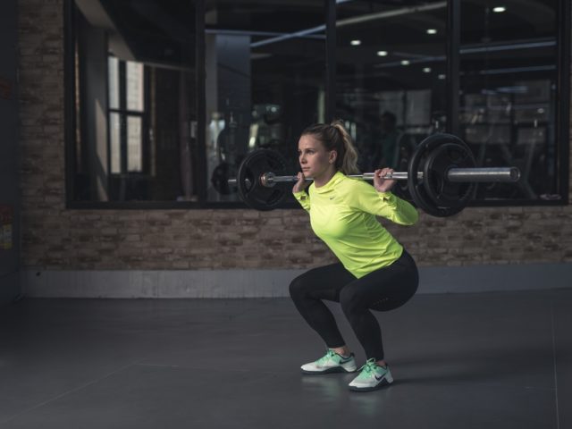 Woman squatting with bar weight on her back in gym