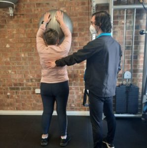 Lady exercising with exercise ball reaching overhead. Health professional correcting technique. 