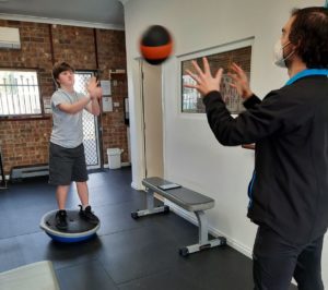 Young man with down syndrome standing on balance ball throwing ball with exercise physiologist