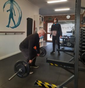 Man lifting weight in gym being watched by exercise physiologist