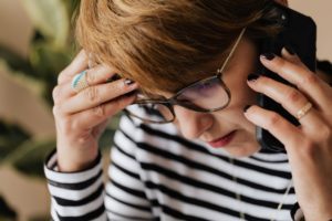 lady wearing black and white striped shirt and glasses on phone looking stressed