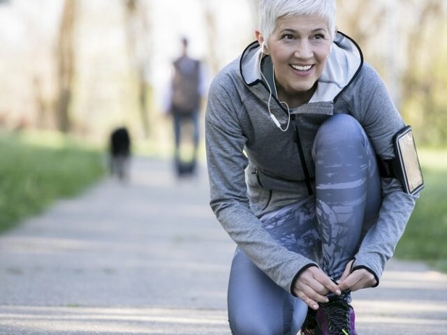 Woman kneeling to tie sho laces on a path in running clothes.