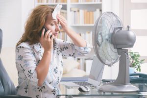Lady feeling hot sitting in front of a fan while working at her desk. Hot Flush. 