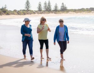 Three active ladies walking along a beach barefoot.