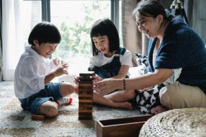 Lady sitting on the floor playing with two children with blocks.