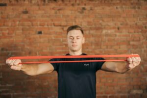 Man holding orange exercise band pressing arms to side