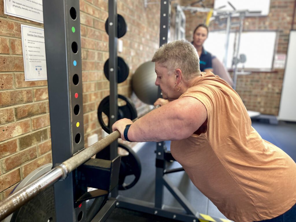 Woman in gym doing push up leaning on bar squat rack
